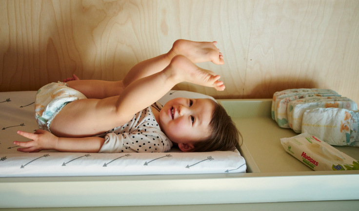 Toddler laying on her back and playing with her legs in the air