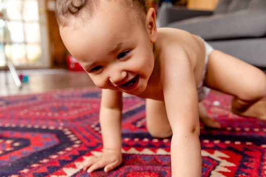 A laughing baby wearing a Huggies Little Movers Plus Diaper crawls on a rug